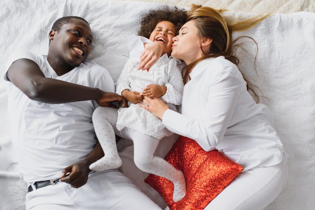 Parents chahutant avec leur petite fille dans un lit