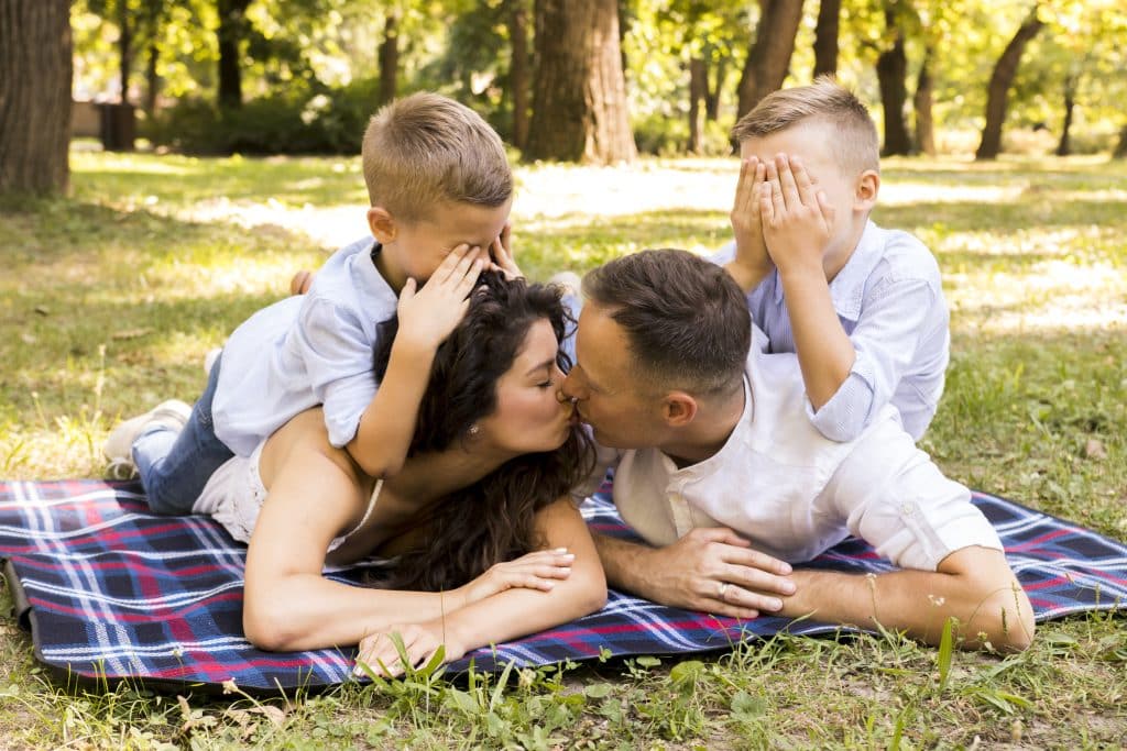Couple allongé dans l'herbe avec leurs enfants qui grimpent sur leur dos