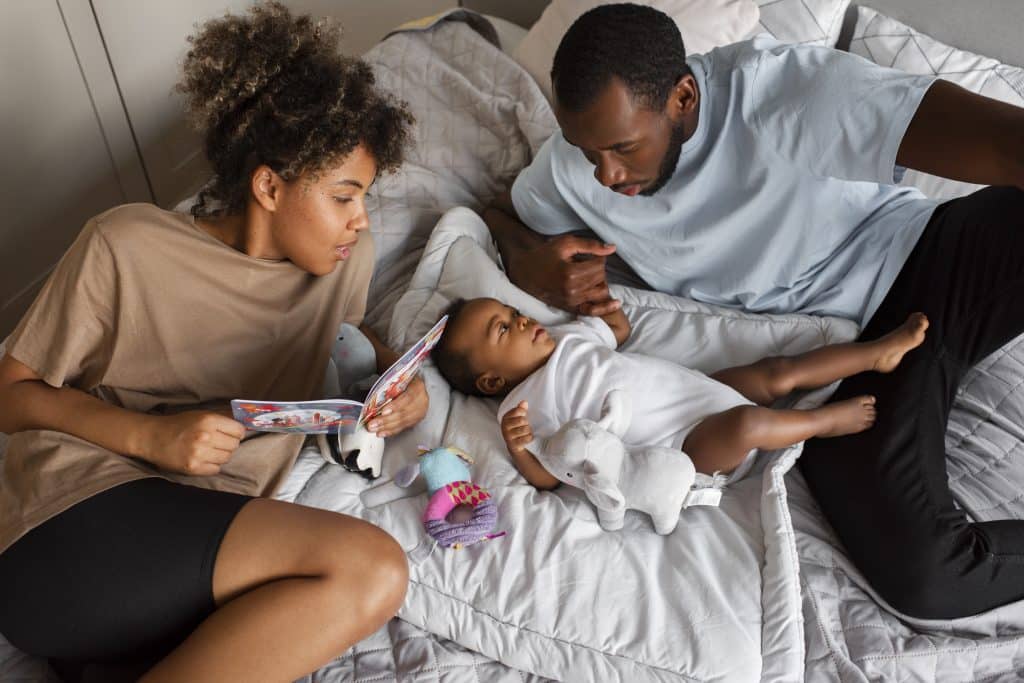 Bébé allongé sur le lit entre ses jeunes parents.