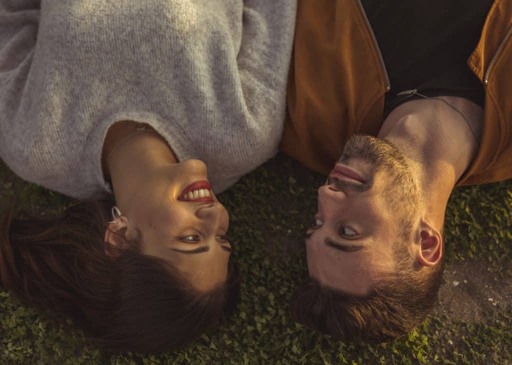Vue en plongée d'un couple allongé dans l'herbe qui se regarde.