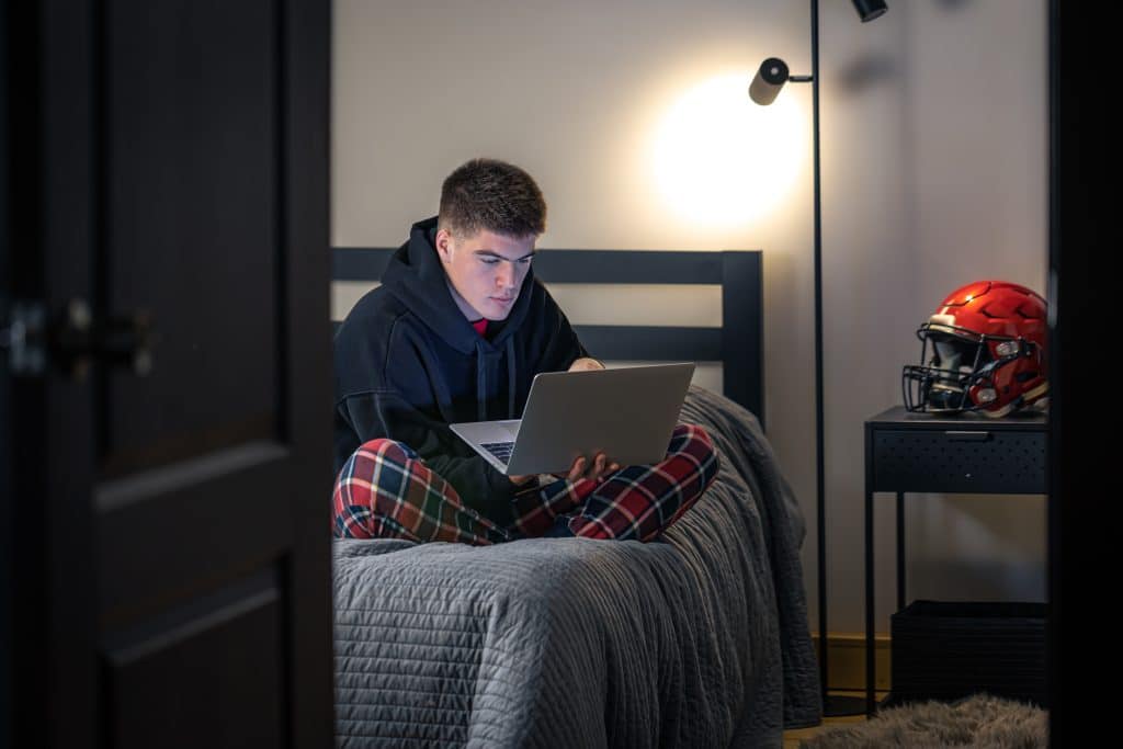 Ado assis en tailleur sur son lit et regardant son ordinateur.
