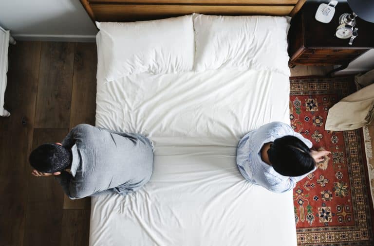 vue en plongée d'un lit conjugal, chacun des époux étant assis d'un côté du lit et se tournant le dos.