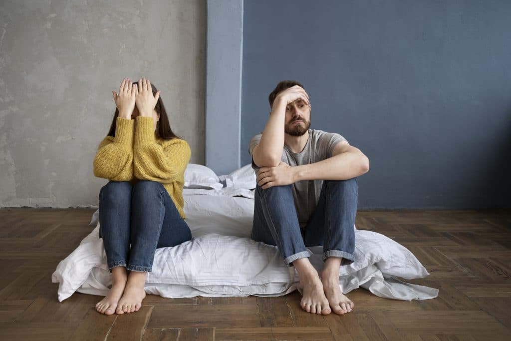 couple assis à terre après une dispute, chacun ayant le visage dans les mains.