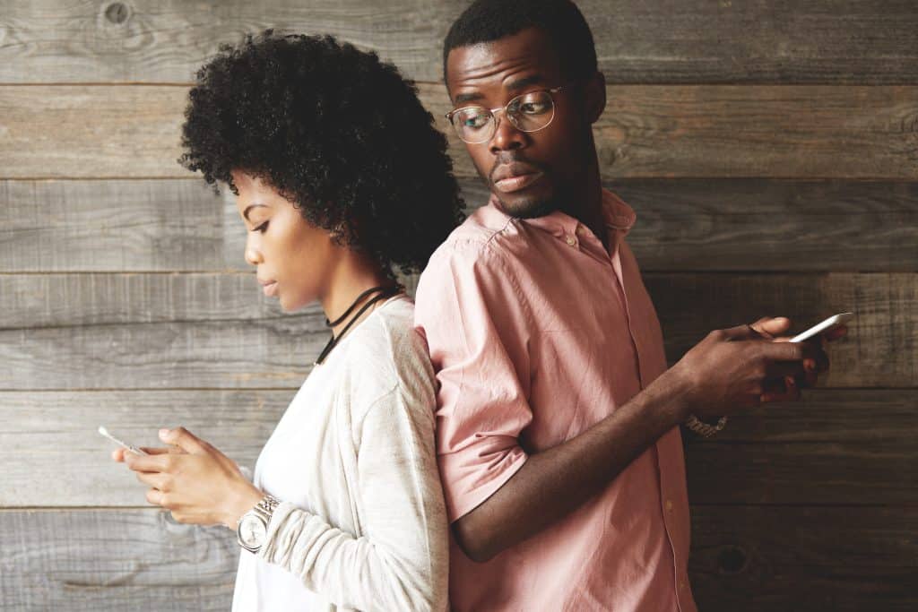 couple dos à dos, la femme regarde son téléphone et l'homme regarde par-dessus son épaule ce que texte sa femme.