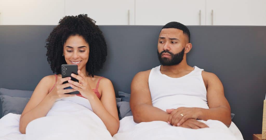 couple assis dans le lit, l'homme regardant sa femme qui rigole en envoyant des textos.